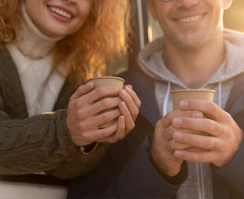 Portrait of joyful young woman enjoying a cup of coffee at home. Smiling pretty girl drinking hot tea in front of the window in winter. Excited woman wearing spectacles and sweater and laughing in an autumn day.