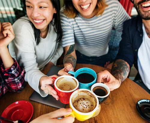 Portrait of joyful young woman enjoying a cup of coffee at home. Smiling pretty girl drinking hot tea in front of the window in winter. Excited woman wearing spectacles and sweater and laughing in an autumn day.